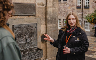 Tour guide explaining a historical plaque related to the Witches of Edinburgh.