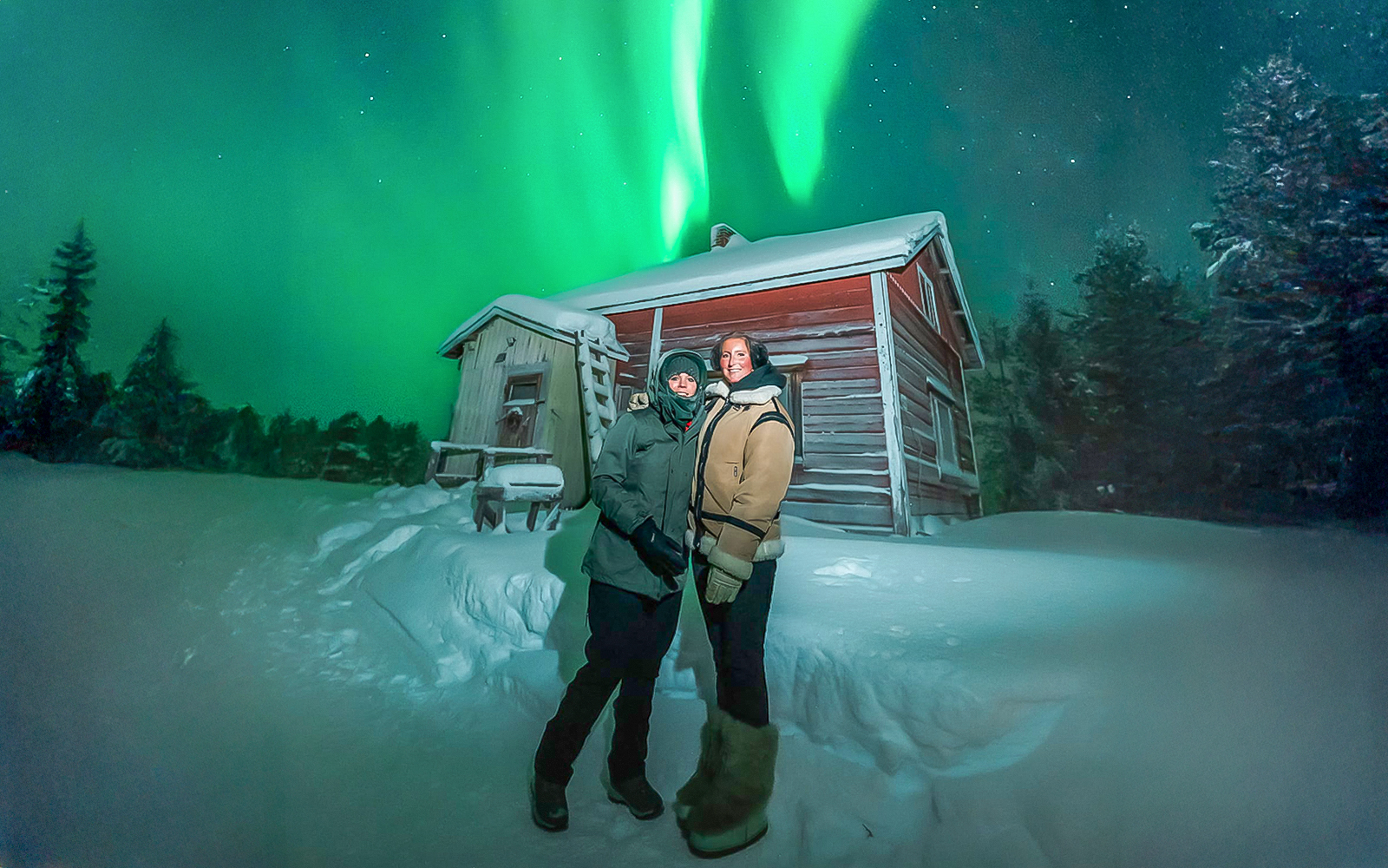 Guests viewing northern lights near a snowy cabin during Northern Lights Big Group Tour.