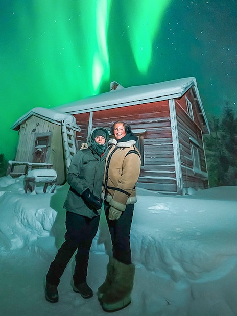 Guests viewing northern lights near a snowy cabin during Northern Lights Big Group Tour.