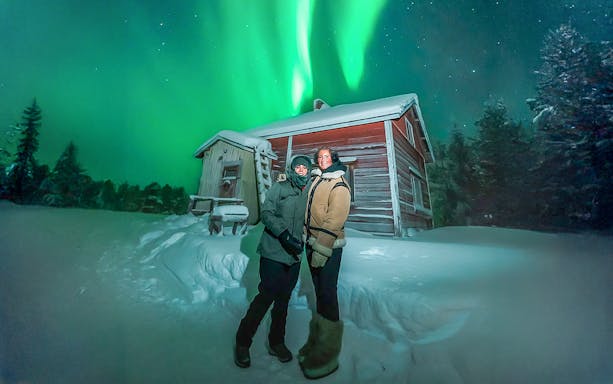 Guests viewing northern lights near a snowy cabin during Northern Lights Big Group Tour.
