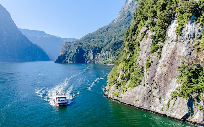 Cruise ship sailing through Milford Sound, New Zealand with towering cliffs and lush greenery.