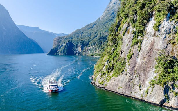 Cruise ship sailing through Milford Sound, New Zealand with towering cliffs and lush greenery.