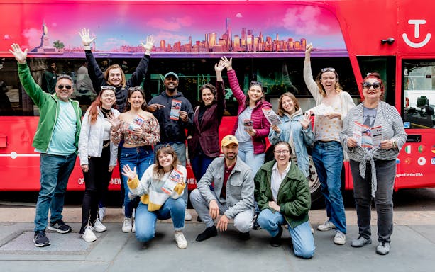 Group of tourists with Hop-On Hop-Off Pass in front of a red tour bus in New York City.