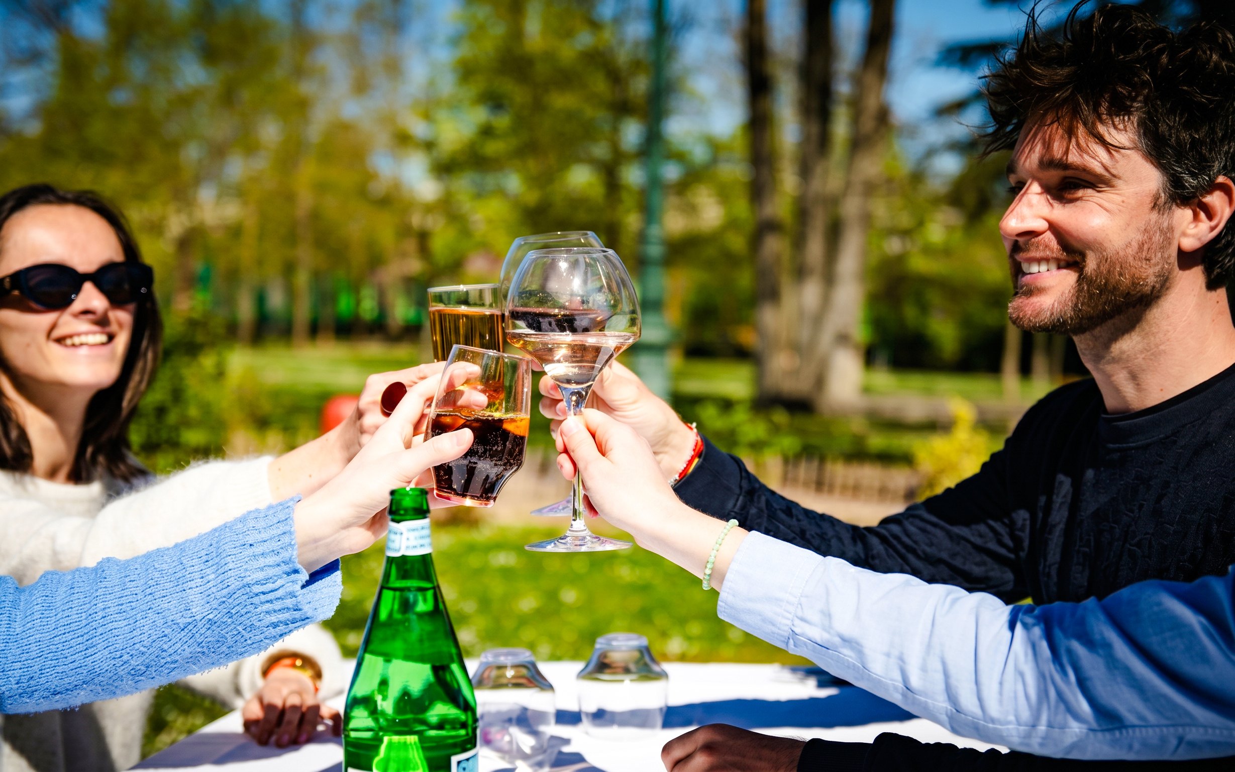 People toasting drinks at a table in Jardin d'Acclimatation, Paris.