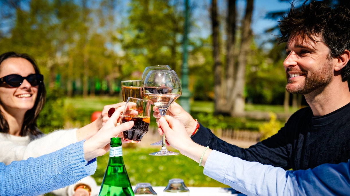 People toasting drinks at a table in Jardin d'Acclimatation, Paris.
