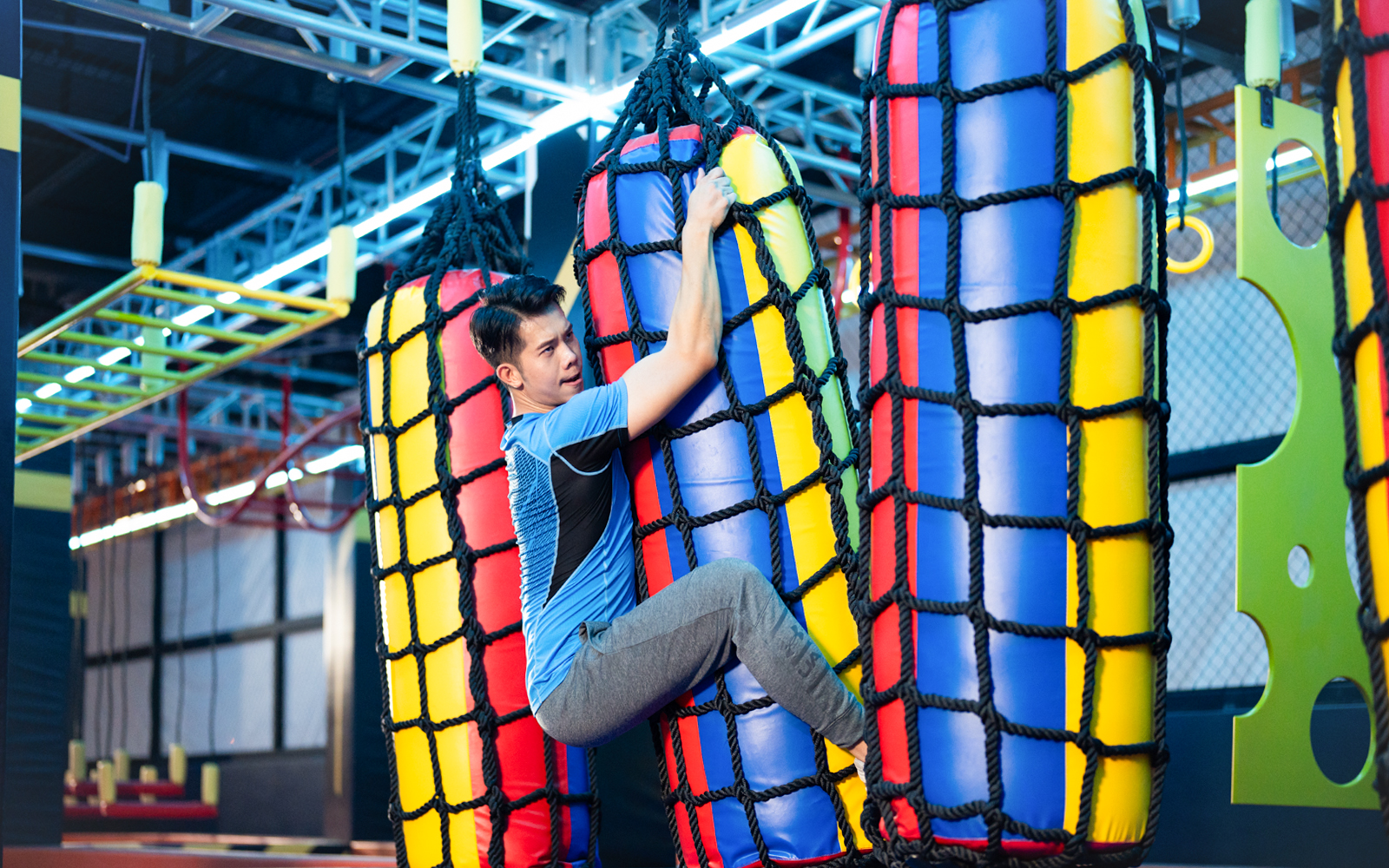 Man climbing colorful rope bag in indoor adventure park.