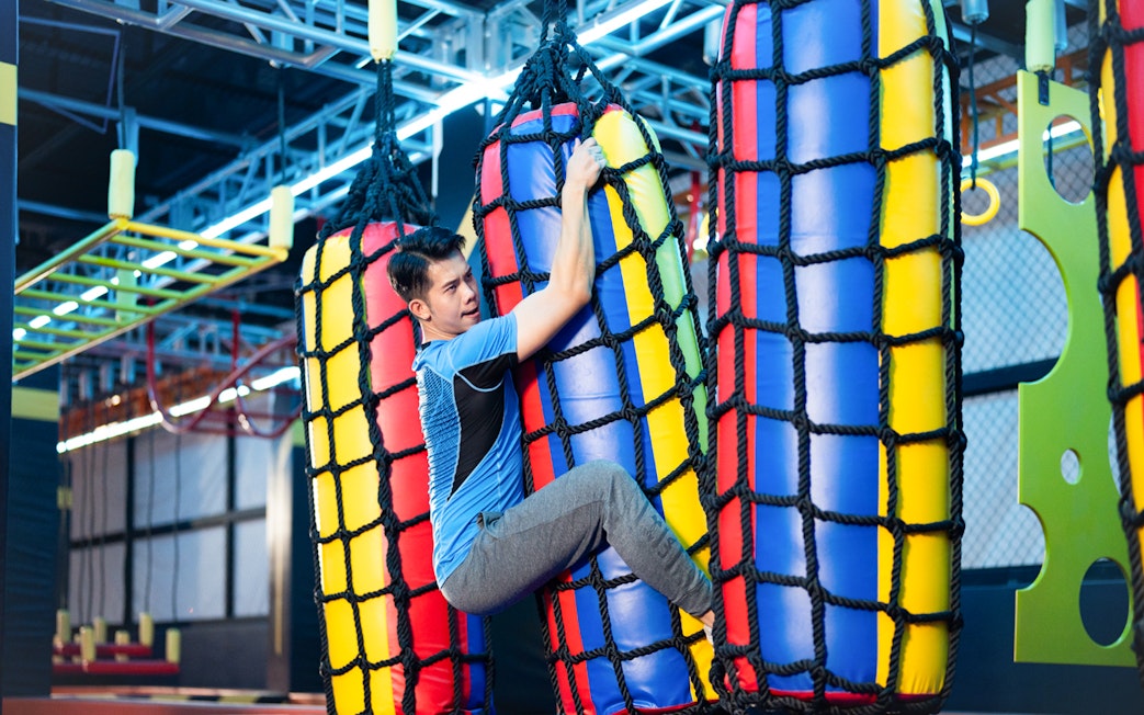 Man climbing colorful rope bag in indoor adventure park.