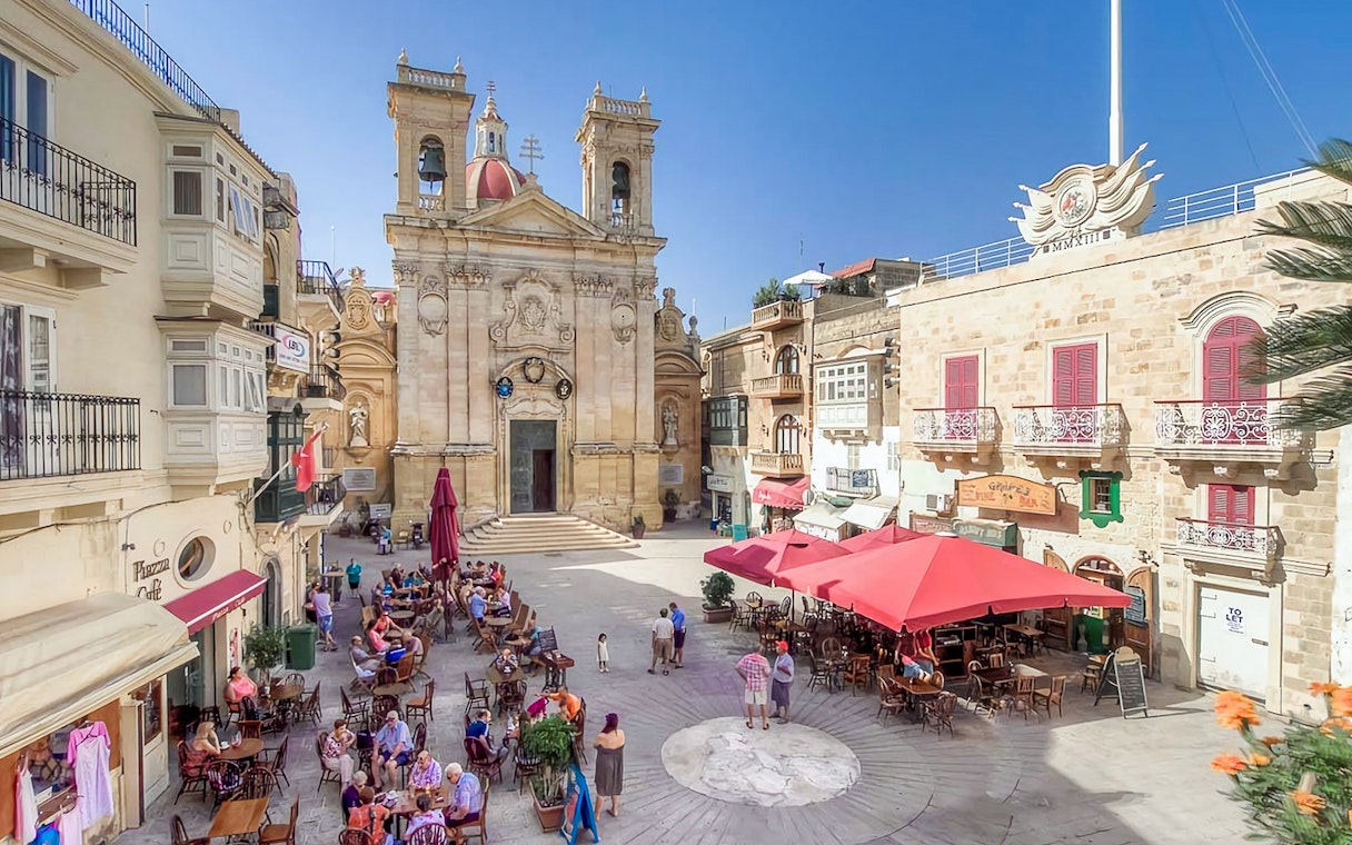 Gozo town square with outdoor cafes and historic church on a sunny day.