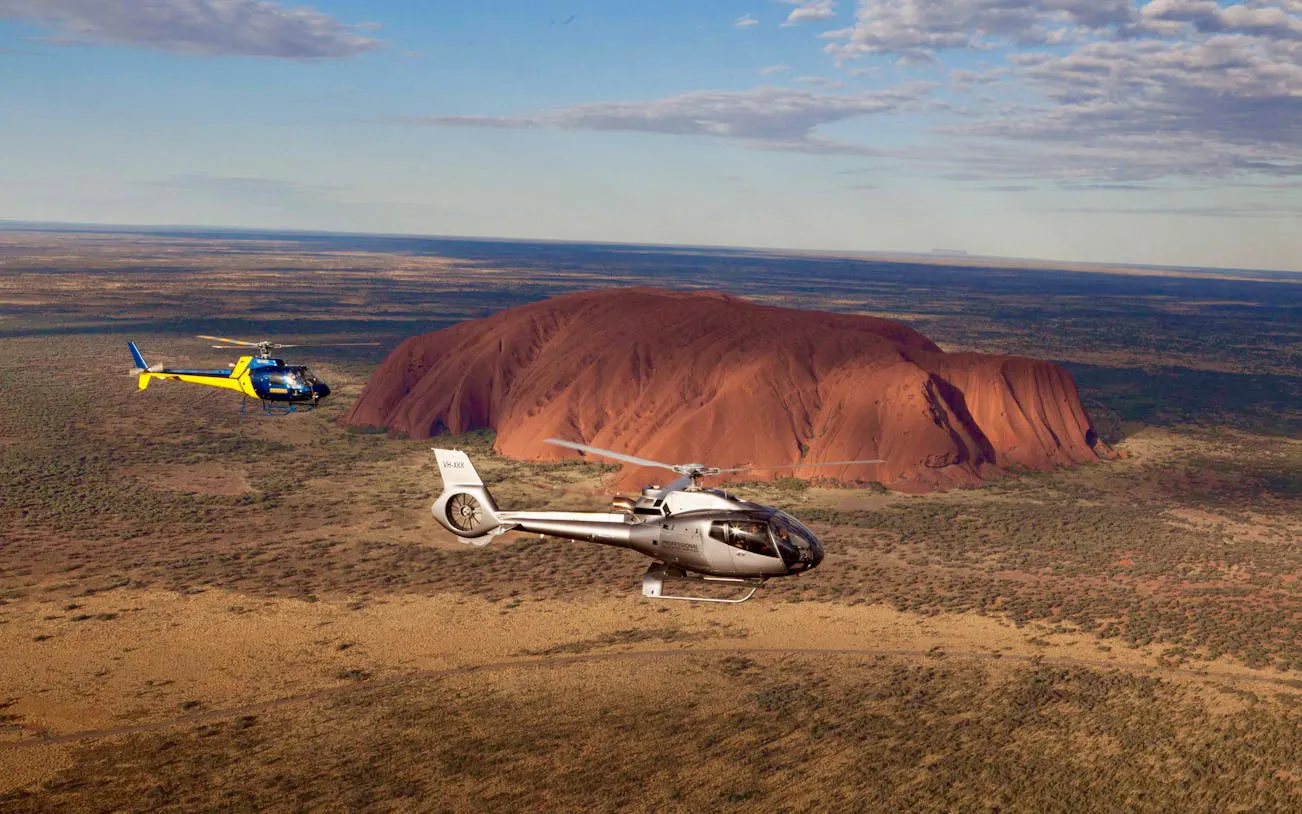 Helicopters flying over Uluru in Australia during a scenic tour.