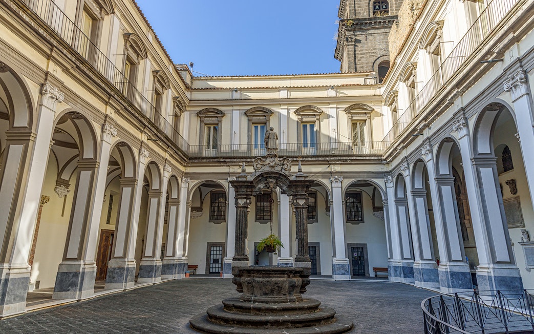 Cloister of San Lorenzo Maggiore in Naples with arched colonnades and central statue.