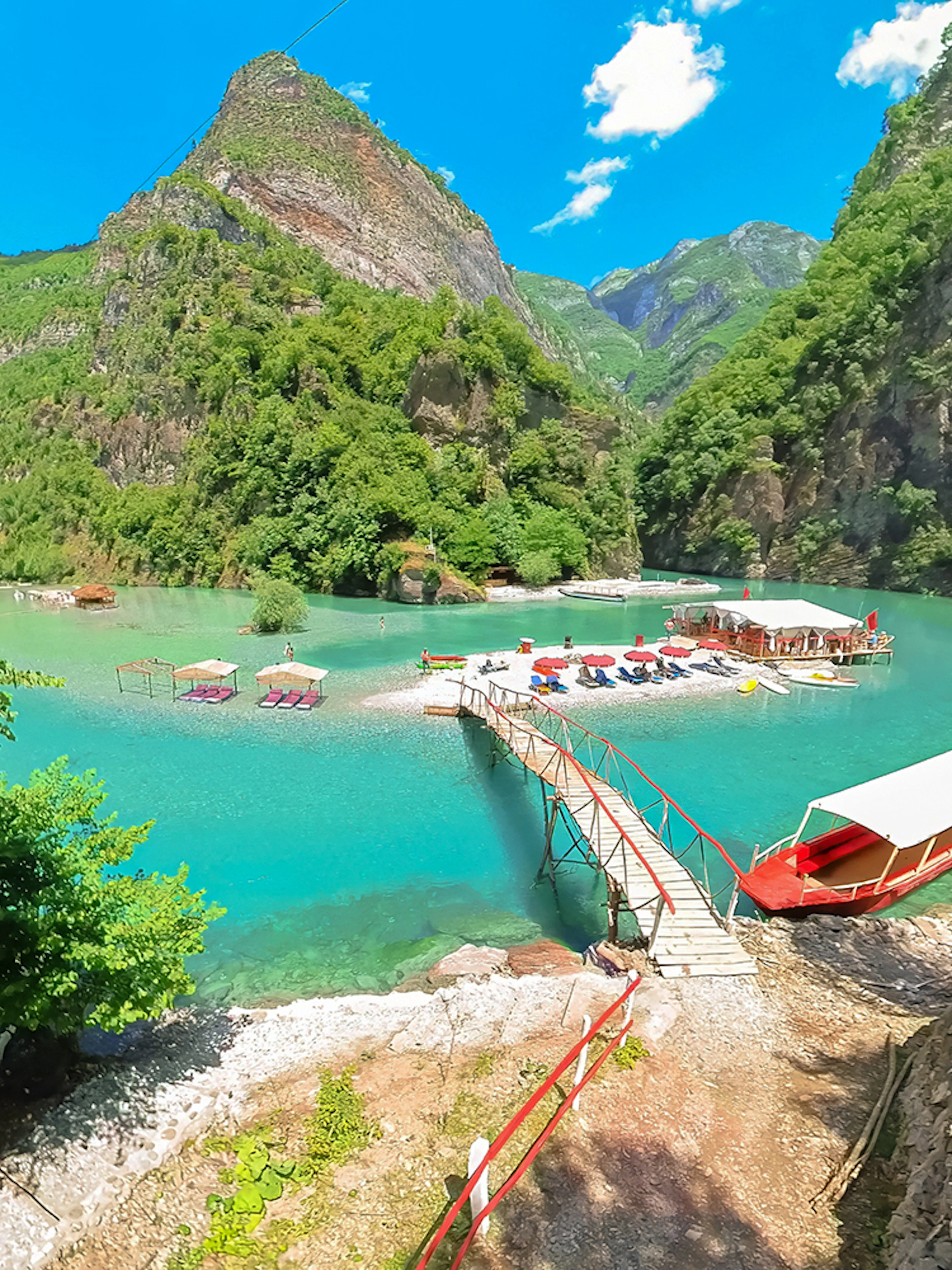 Komani Lake view with boats and dock on the Shala River, surrounded by lush mountains.