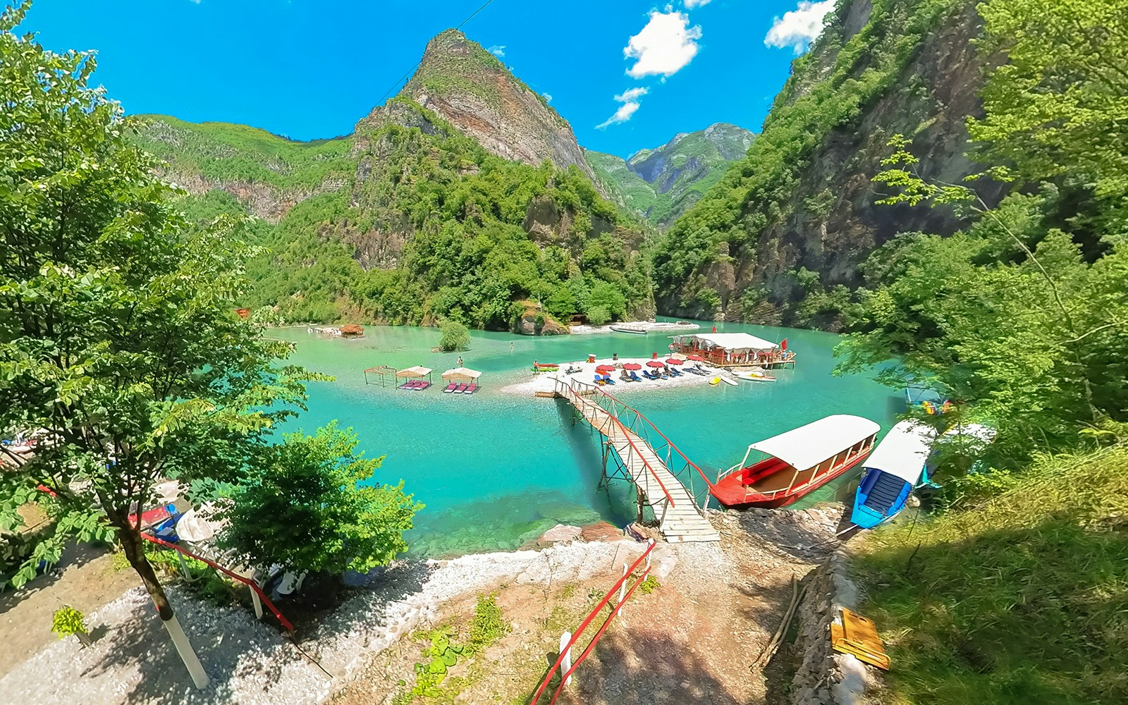 Komani Lake view with boats and dock on the Shala River, surrounded by lush mountains.