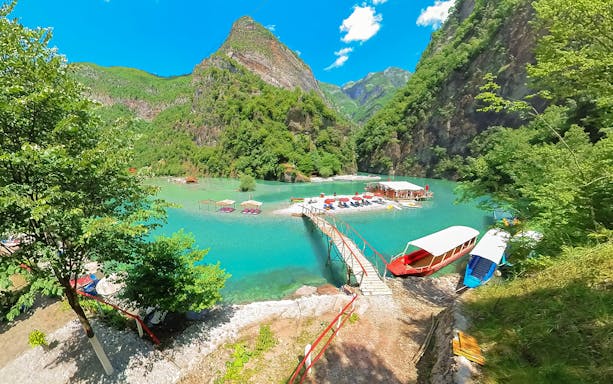 Komani Lake view with boats and dock on the Shala River, surrounded by lush mountains.