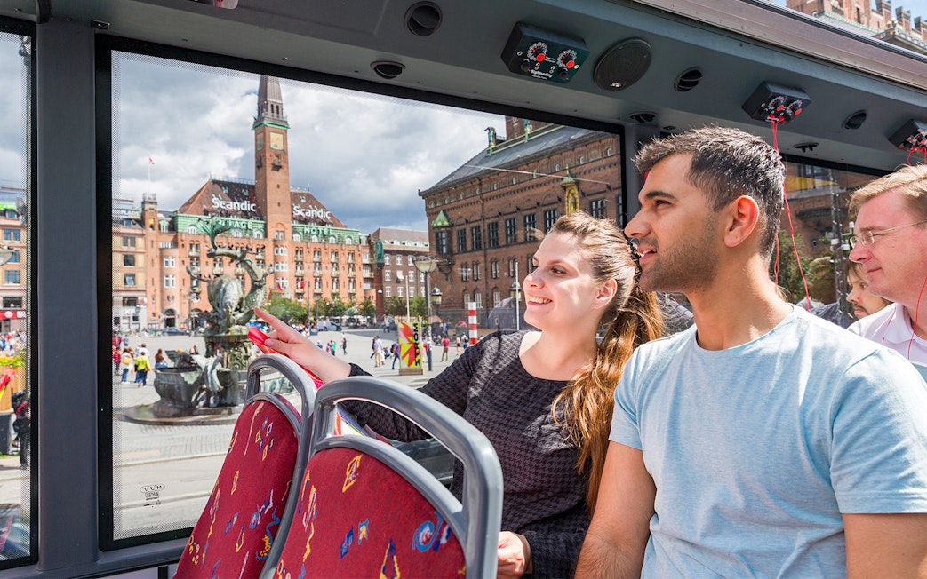 Couple enjoying Copenhagen Hop-On-Hop-Off bus tour with city square view.