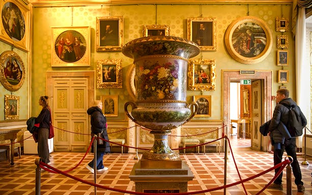 Palazzo Pitti interior with large decorative vase and visitors viewing art in Florence.