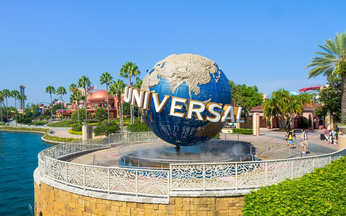 Universal globe at Universal Studios Resort, Orlando, with surrounding palm trees and visitors.