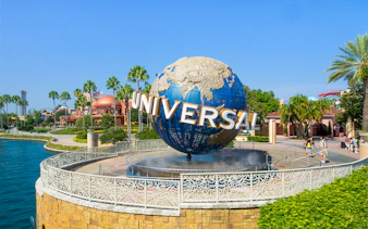 Universal globe at Universal Studios Resort, Orlando, with surrounding palm trees and visitors.