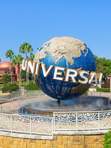 Universal globe at Universal Studios Resort, Orlando, with surrounding palm trees and visitors.