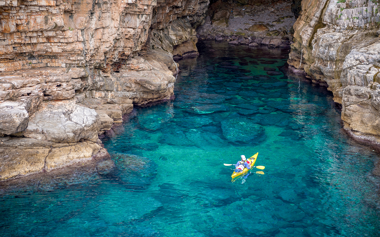Kayakers exploring Betina Cave's clear waters at sunset.