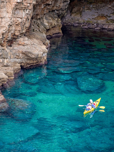 Kayakers exploring Betina Cave's clear waters at sunset.