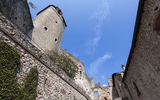 Stone walls and tower of Avio Castle under a clear blue sky.