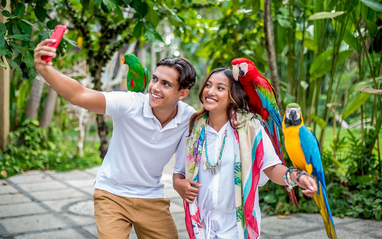 Visitors taking a selfie with colorful parrots at Bali Bird Park.