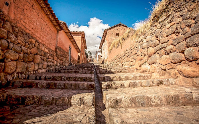 Stone stairway through village in Sacred Valley, Peru, with rustic walls and blue sky.