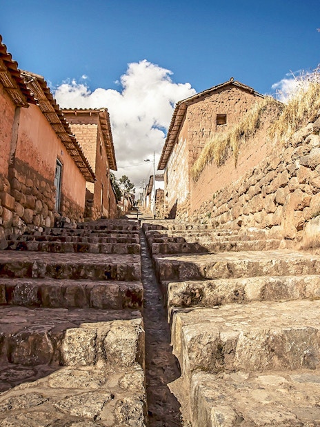 Stone stairway through village in Sacred Valley, Peru, with rustic walls and blue sky.