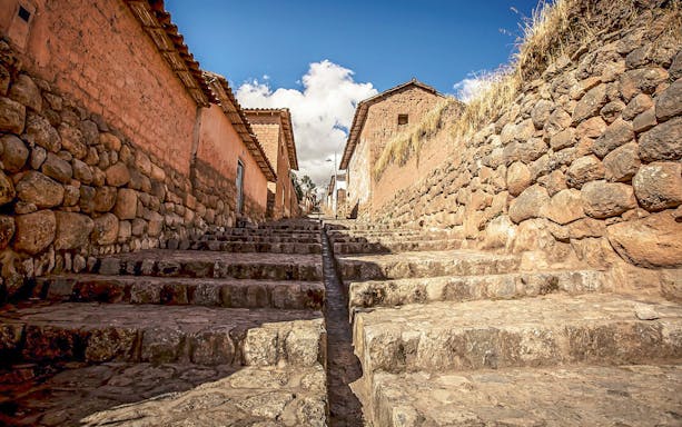 Stone stairway through village in Sacred Valley, Peru, with rustic walls and blue sky.