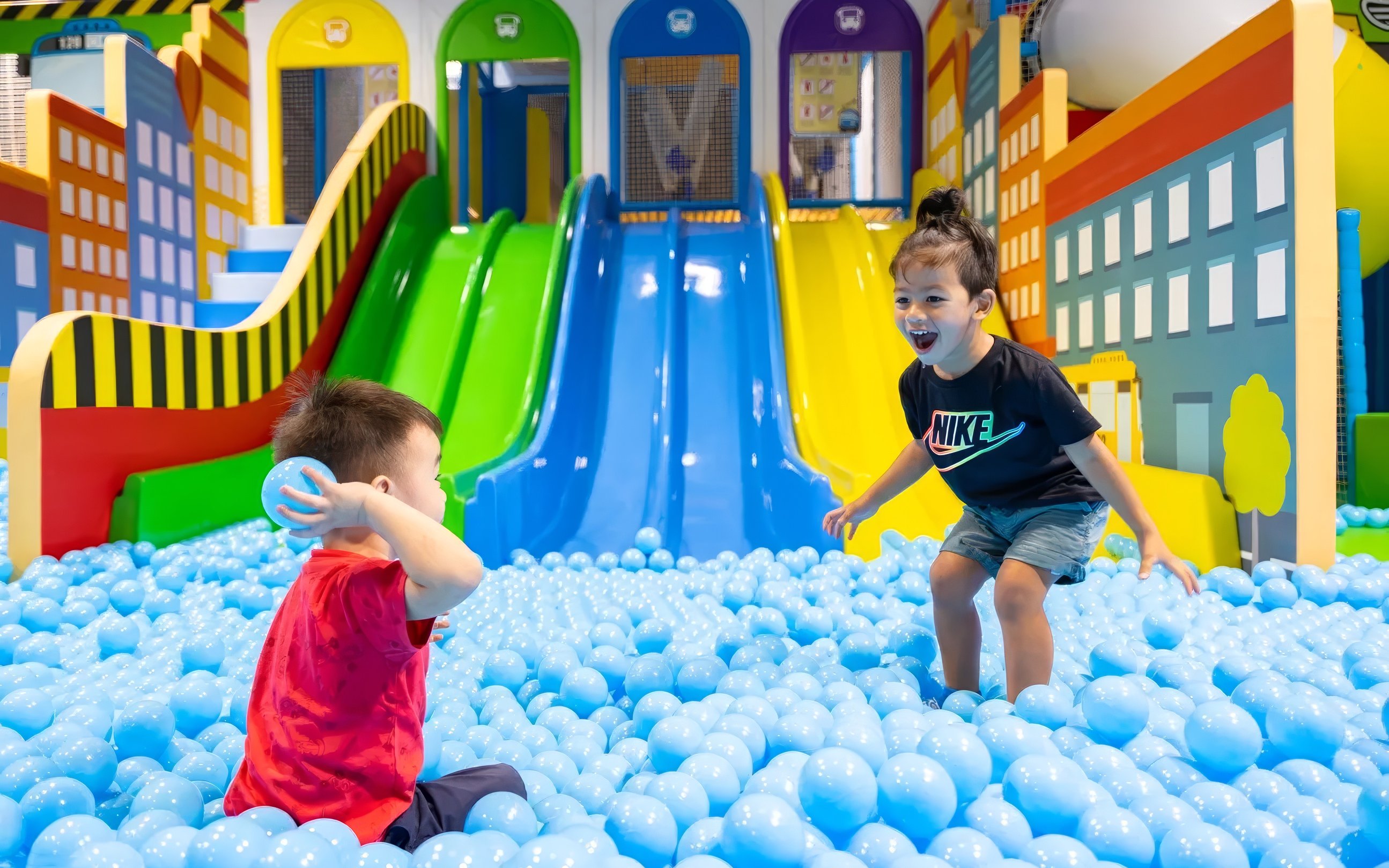 Children playing in a ball pit at Tayo Station with colorful slides in the background.