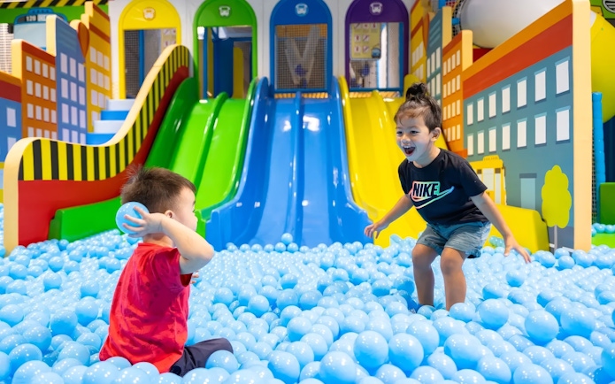 Children playing in a ball pit at Tayo Station with colorful slides in the background.