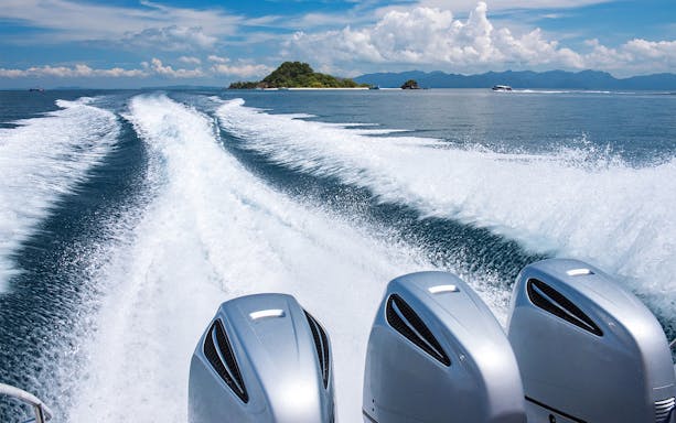 Speedboat leaving wake near Khai Islands, Phuket, with distant islands and clear sky.