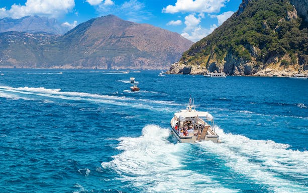 Boat approaching Capri's Blue Grotto with scenic coastal view.