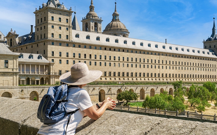 Woman with hat and backpack viewing San Lorenzo de El Escorial monastery.