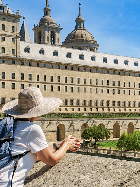 Woman with hat and backpack viewing San Lorenzo de El Escorial monastery.