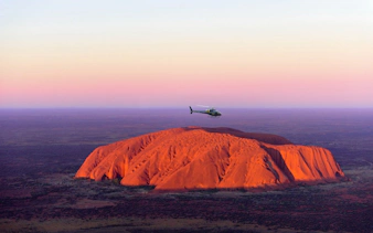 Helicopter flying over Uluru at sunset, Australia.