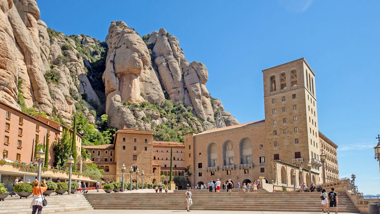 Montserrat Monastery exterior with tourists and rocky mountain backdrop.