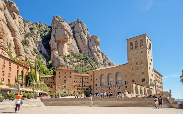 Montserrat Monastery exterior with tourists and rocky mountain backdrop.