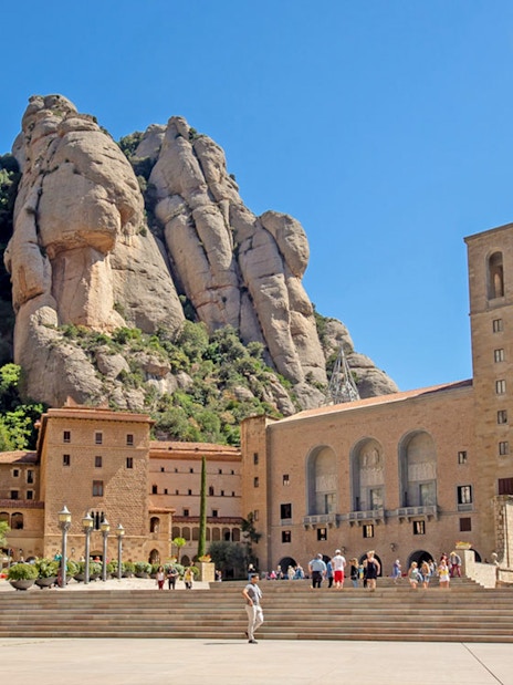 Montserrat Monastery exterior with tourists and rocky mountain backdrop.