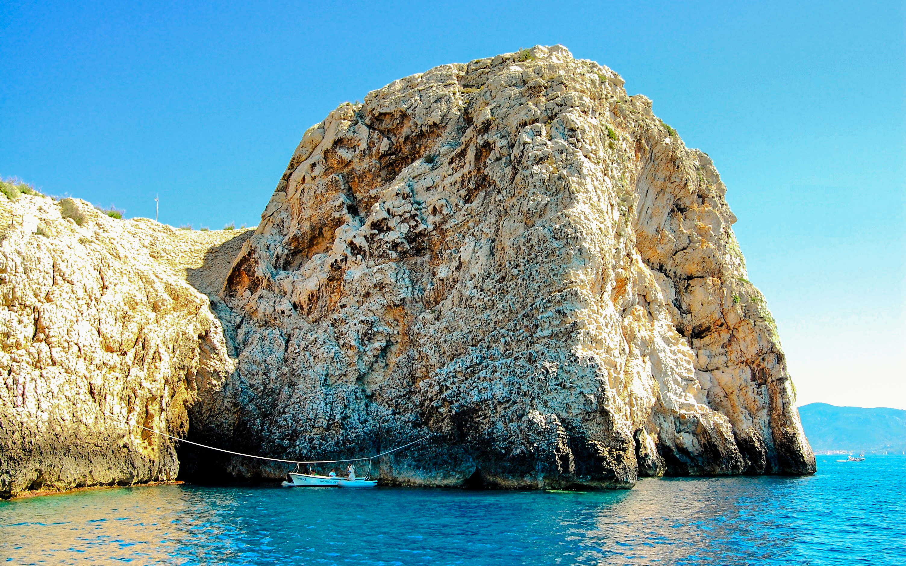 Bisevo Island Blue Cave entrance with boat on clear water.