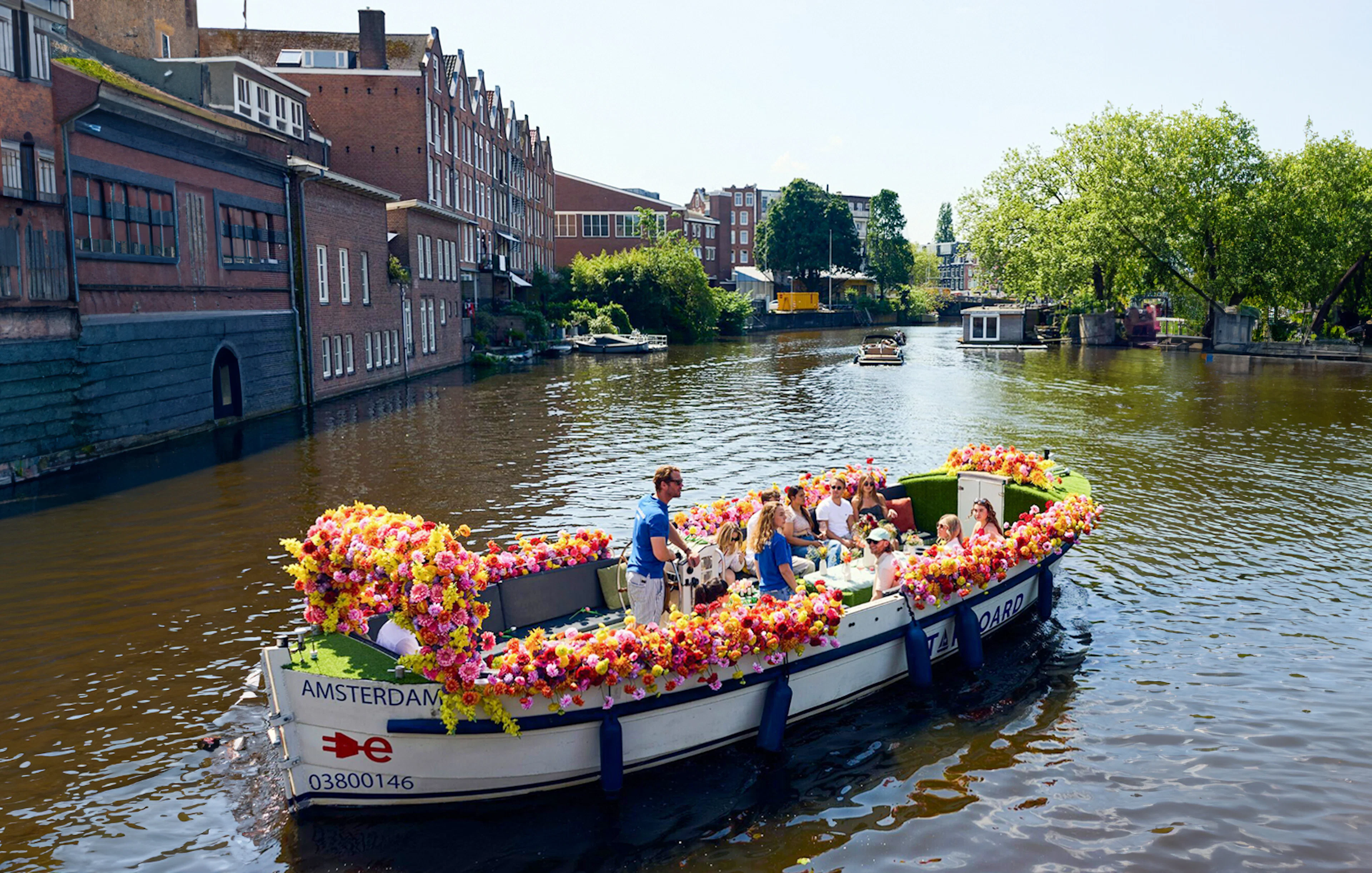 Amsterdam canal cruise on a flower-adorned boat with passengers enjoying the view.