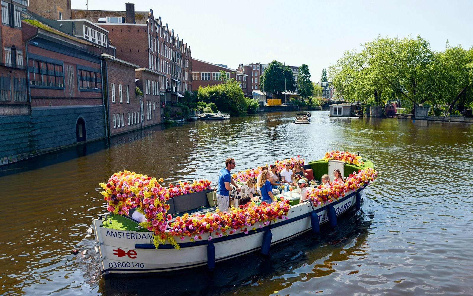 Amsterdam canal cruise on a flower-adorned boat with passengers enjoying the view.