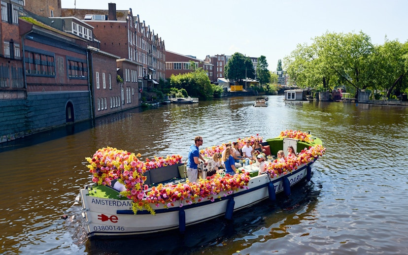 Amsterdam canal cruise on a flower-adorned boat with passengers enjoying the view.