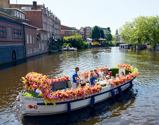 Amsterdam canal cruise on a flower-adorned boat with passengers enjoying the view.