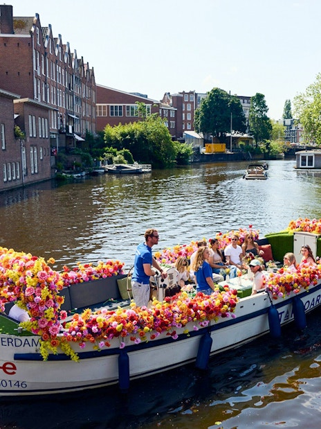 Amsterdam canal cruise on a flower-adorned boat with passengers enjoying the view.