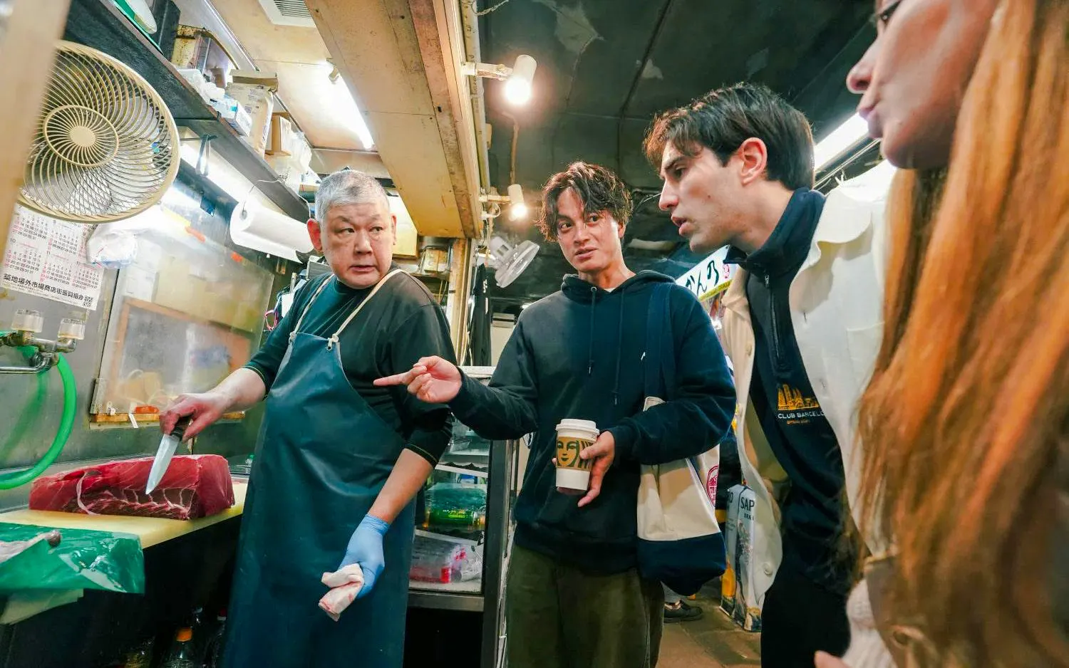 Tourists observing a chef preparing fish at Tsukiji Fish Market kitchen stall.