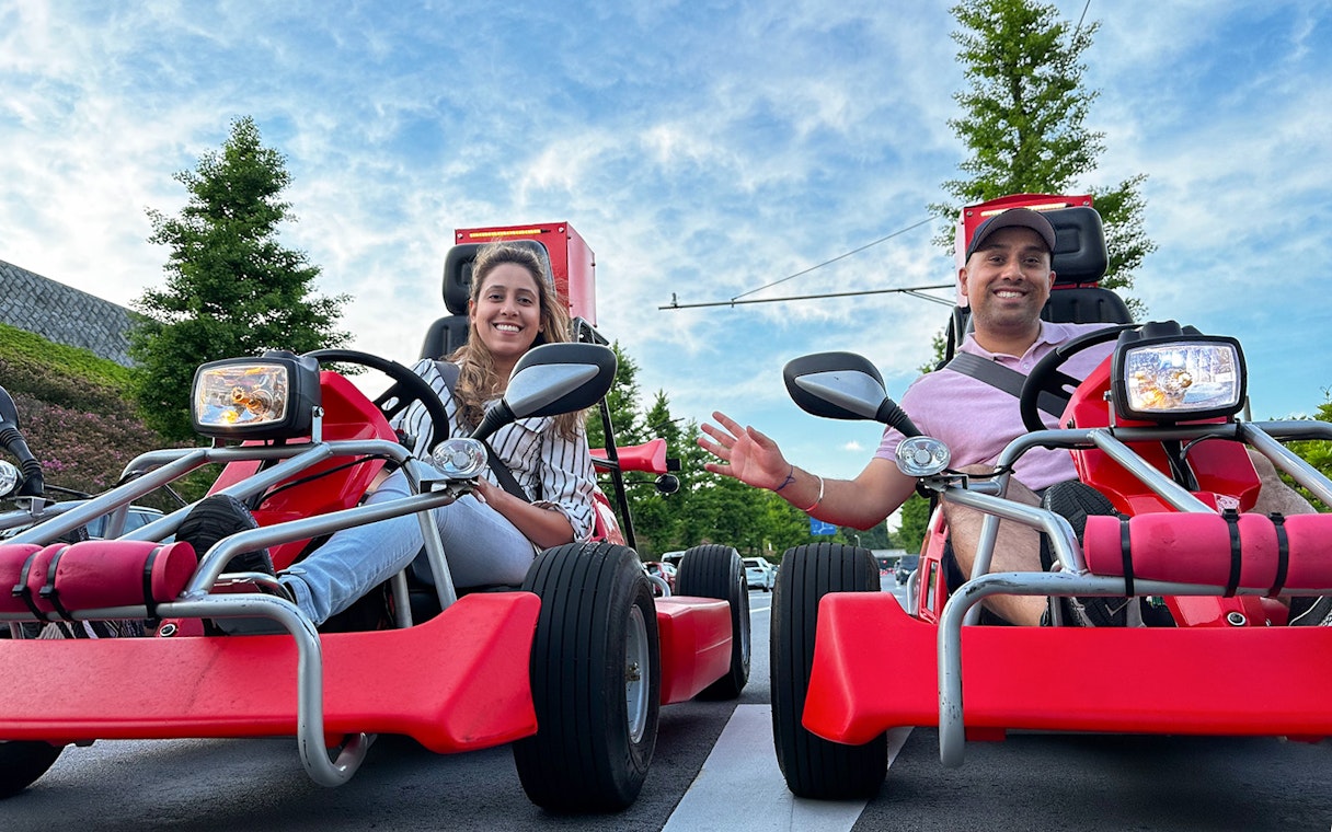 Two people smiling in red go-karts during a Shibuya street go-kart experience.