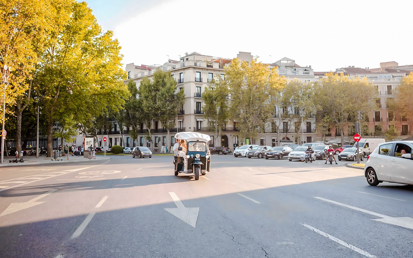 Electric tuk-tuk driving through a tree-lined street in Madrid.