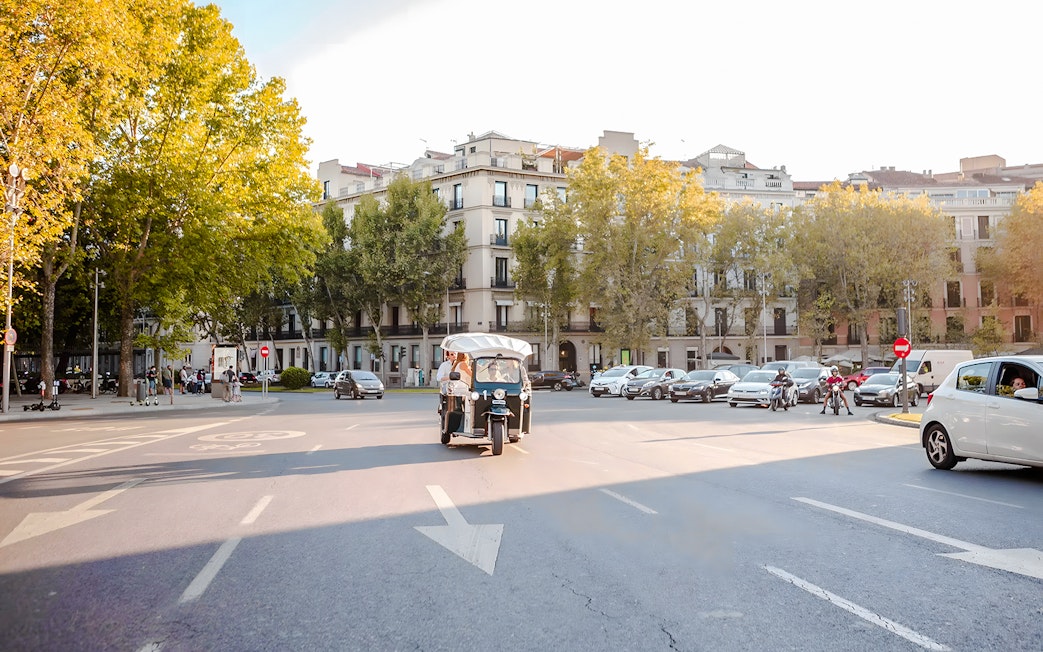 Electric tuk-tuk driving through a tree-lined street in Madrid.