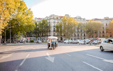 Electric tuk-tuk driving through a tree-lined street in Madrid.